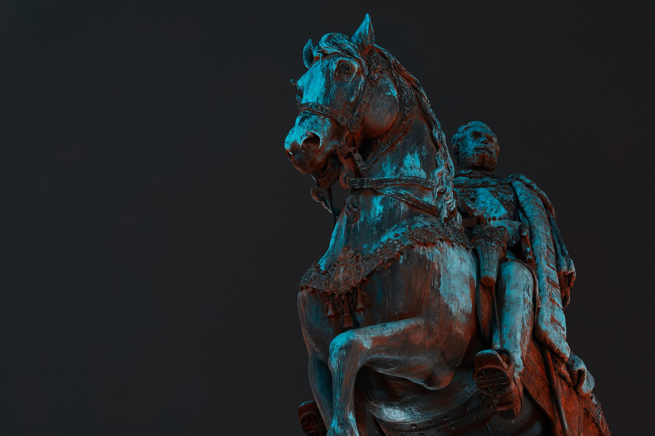 A bronze horse and rider lit in turquoise and warm red against the night sky.